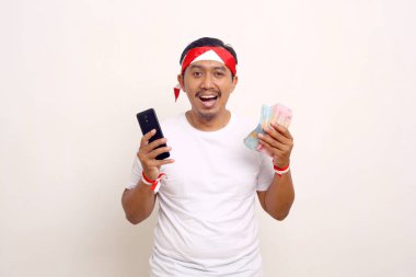 Mutlu Asyalı adam elinde cep telefonu ve Endonezya parası tutarken ayakta duruyor. Bağımsızlık Günü kavramı