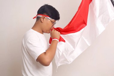 Asian boy is kissing an Indonesian flag. Independence day concept. Isolated on white with copyspace