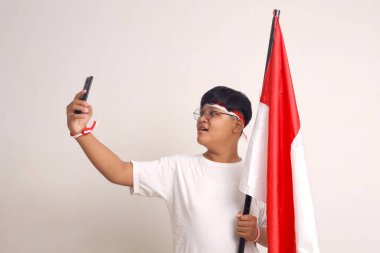 Endonezya bayrağı tutarken ve selfie çekerken mutlu Asyalı çocuk. Beyazda izole edilmiş