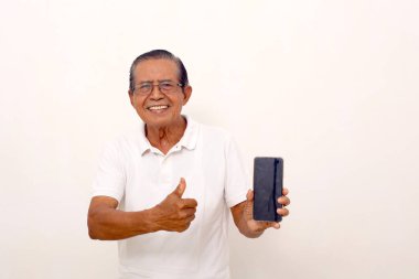 Asian old man standing while holding a cell phone and showing thumbs up. Isolated on white