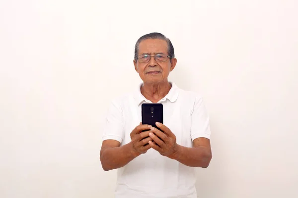 Calm Elderly Asian Man Standing While Holding Cell Phone Isolated — стоковое фото