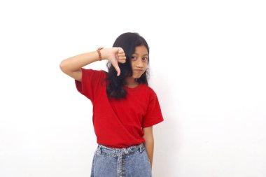 Unhappy asian little girl standing while showing thumbs down. Dislike concept. Isolated on white