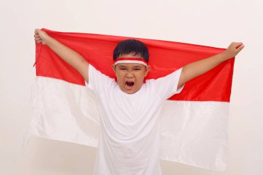 Happy asian boy standing while carrying indonesian flag. Independence day concept. Isolated on white