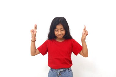 Asian little girl standing while making hope hand gesture and close eyes. Isolated on white