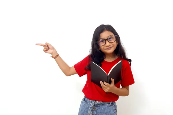 Happy Asian Schoolgirl Standing While Holding Book Pointing Sideways Isolated — Stock Photo, Image