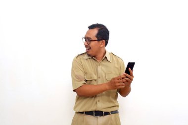 Indonesian government employees standing while looking to side and holding a cell phone.