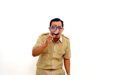 Happy Indonesian government employees standing while looking at the camera through a magnifying glass