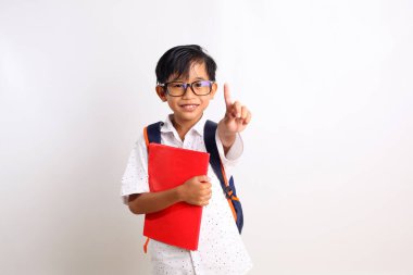 Asyalı mutlu okul çocuğu, elinde kitap ve okul çantasıyla beni işaret ediyor.