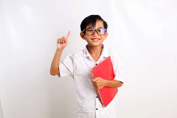 Šťastný Asijský Chlapec Stojící Ukazující Prstem Nesoucí Knihu Izolováno Bílém — Stock fotografie