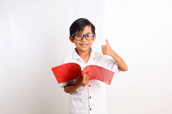 Chytrý Asijský Školák Který Nosí Knihu Zatímco Ukazuje Palce Nahoru — Stock fotografie