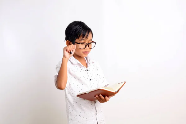 本とペンを持ちながら考える賢いアジア系の少年 白地に隔離された — ストック写真