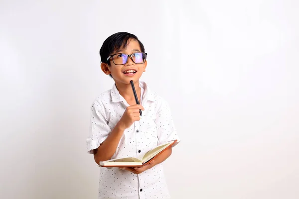 Щасливий Азіатський Школяр Думає Тримаючи Книгу Дивлячись Вгору Ізольовані Білому — стокове фото