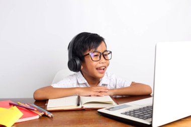 Mutlu Asyalı ilkokul çocuğu evde dizüstü bilgisayar kullanarak online çalışıyor. Beyaz arkaplanda izole
