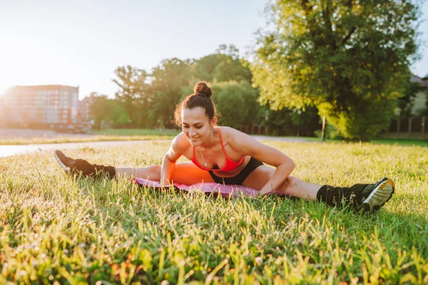 Positive woman in sport wear in park do stretching workout on mat