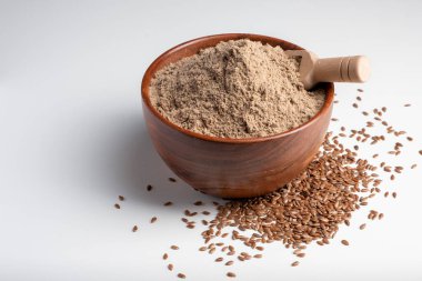 Çiğ keten tohumu unu ahşap bir kasede beyaz arka planda..