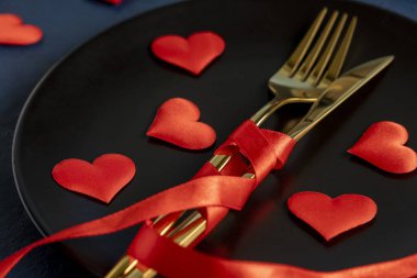 Sevgililer günü masasında koyu mavi bir arka plan. Siyah tabak, altın çatal bıçak takımı, kırmızı kalp, romantik yemek konsepti.