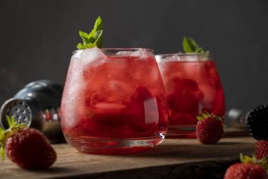 Çilekli, buzlu ve naneli kırmızı içecek. Tahta masadaki bardakta serinletici yaz kokteyli.