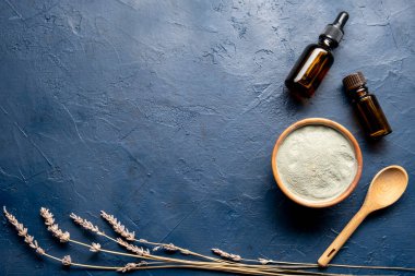 Mavi arka planda aroma yağı olan ahşap bir kasede kozmetik yeşil kil. Doğal kozmetik konsepti.