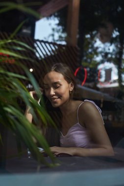 Gülümseyen güzel bayan telefonla arıyor. Kafenin dışındaki cam kırıklarından vurulmuş.