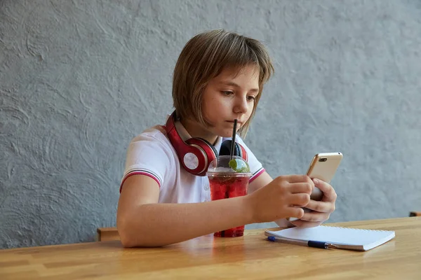 ヘッドフォンと赤い氷のレモネードを持つ女子高生は、スマートフォン、サーフインターネットを使用しています — ストック写真