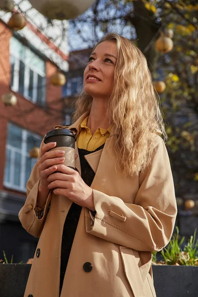 Kaukasiska leende kvinna i beige trenchcoat hålla kopp kaffe utomhus — Stockfoto