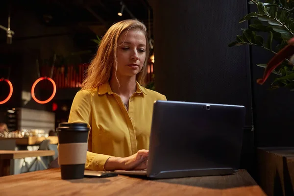 Νεαρή ελκυστική ξανθιά καυασιάτισσα που κάθεται στην καφετέρια, και δουλεύει σε φορητό υπολογιστή — Φωτογραφία Αρχείου