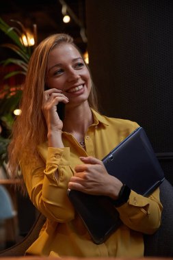 Akıllı telefondan arayan çekici bir kadın. Kafede dizüstü bilgisayarını tutuyor.