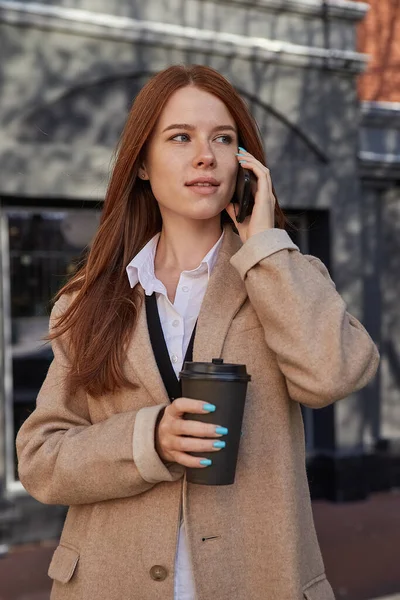Kaukasiska kvinna i snygg beige rock ringer via smartphone, dricka kaffe — Stockfoto