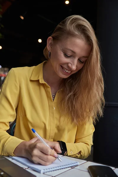 Όμορφη νεαρή καυκάσια επιχειρηματίας γράφει σημειώσεις στο σημειωματάριο στο καφέ — Φωτογραφία Αρχείου