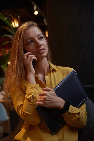 Ελκυστική καυασιάτισσα γυναίκα καλώντας από το smartphone, κρατώντας φορητό υπολογιστή στα χέρια στο καφέ — Φωτογραφία Αρχείου
