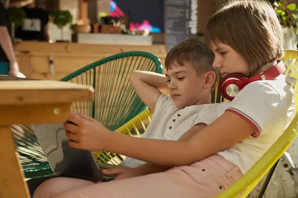 退屈した小さな白人の子供たちは屋外に座ってノートパソコンの画面を見て — ストック写真
