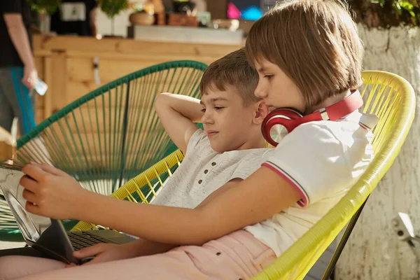 退屈した小さな白人の子供たちは屋外に座ってノートパソコンの画面を見て — ストック写真