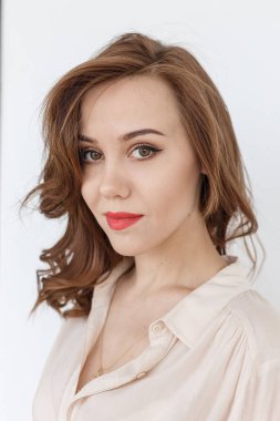 Kırmızı dudaklı, uzun saçlı bej bluzlu genç bir kadın kameraya bakıyor.