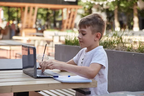 カフェのベランダに座って晴れた日にノートパソコンで勉強する白人少年 — ストック写真
