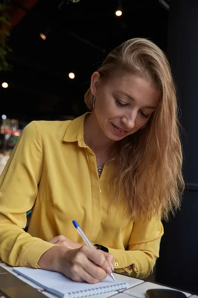 Όμορφη νεαρή καυκάσια επιχειρηματίας γράφει σημειώσεις στο σημειωματάριο στο καφέ — Φωτογραφία Αρχείου