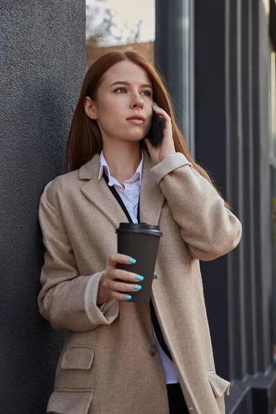 Kaukasiska kvinna i elegant beige rock ringer via smartphone med kopp kaffe — Stockfoto