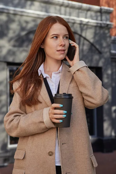 Kaukázusi nő stílusos bézs kabát hívás okostelefonnal, kávézás — Stock Fotó