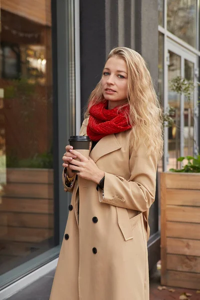 Porträtt av kaukasiska kvinna i beige trenchcoat utomhus med kopp kaffe — Stockfoto