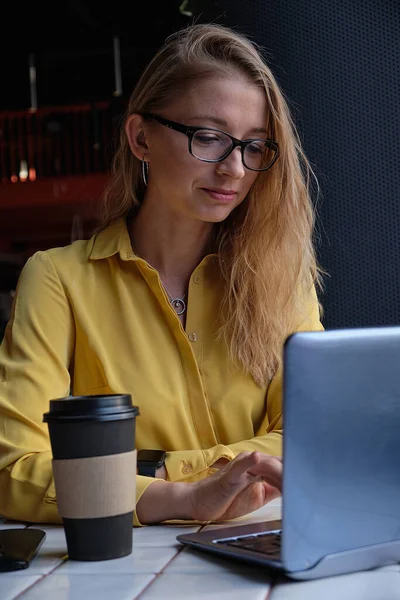 Joven cauasiano bonita mujer sentado en la cafetería, escribiendo en el teclado del ordenador portátil Imágenes de stock libres de derechos