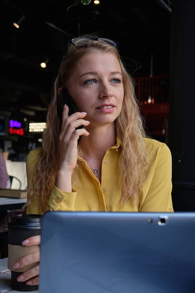 Ung kauasiatisk smuk kvinde på kaffebar med bærbar computer, ringer af smartphone Stock-billede
