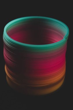 Slinky Rainbow sarmal elastik oyuncak, siyah arka planda, makro yakın 
