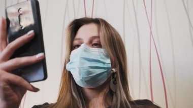 Tıbbi maske takmış genç ve güzel bir kadın videosu arıyor.