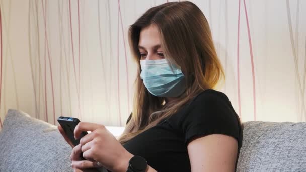 Une femme dans le masque utilise le téléphone à la maison pendant la pandémie Clip Vidéo