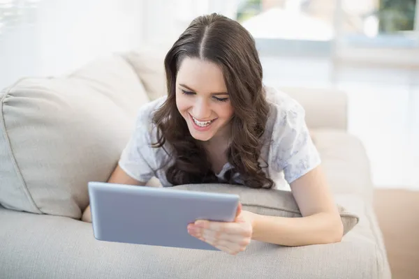 Mujer alegre acostada en un sofá acogedor usando tableta pc —  Fotos de Stock