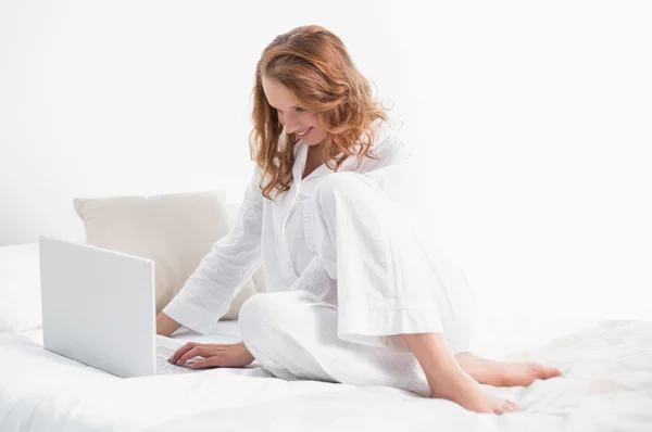 Blij mooie vrouw met behulp van een laptop zitting op haar bed — Stockfoto