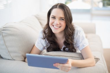 tablet pc tutarak rahat bir kanepede yatan neşeli kadın