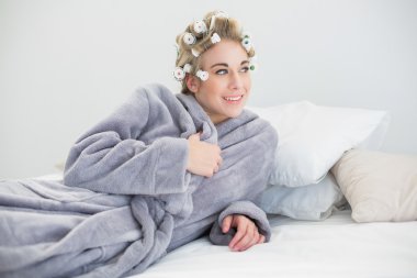 Onu yatakta yatarken poz saç curlers içinde gülümseyen rahatlamış sarışın kadın