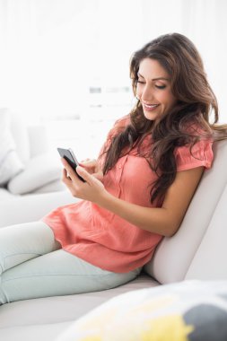 esmer kızın smartphone kullanarak onun kanepede oturan gülümsüyor