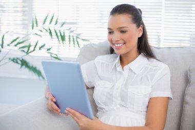 rahat bir koltukta oturan tablet kullanarak gülümseyen güzel kadın