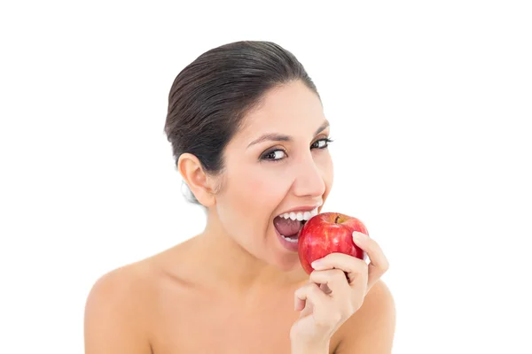 Morena feliz comendo uma maçã vermelha e olhando para a câmera — Fotografia de Stock